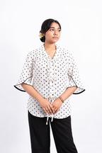The Decords Bella Bow ladies shirt in white with small black motifs, a Cuban collar, three front bow ties and flared sleeves finished with black piping.
