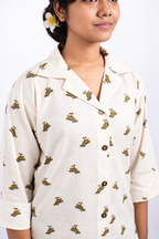 Dino Daze close front view showing the Cuban collar, brown buttons, ivory fabric and small dinosaur motifs.
